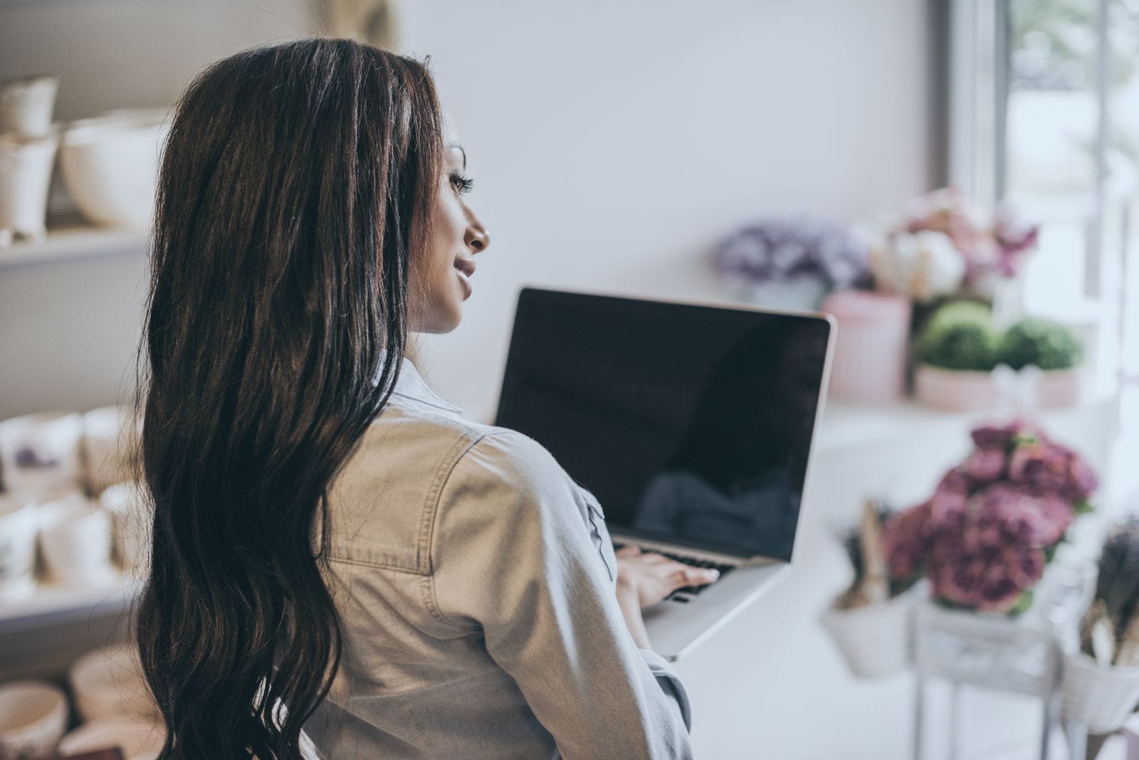 A person at a laptop in a flower shop, seen from behind.